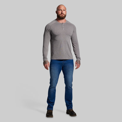 Man wearing a gray long-sleeve shirt and blue jeans on a light gray background