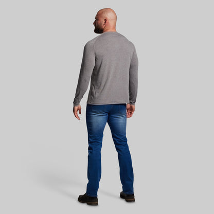 Man wearing a gray long-sleeve shirt and blue jeans on a light gray background