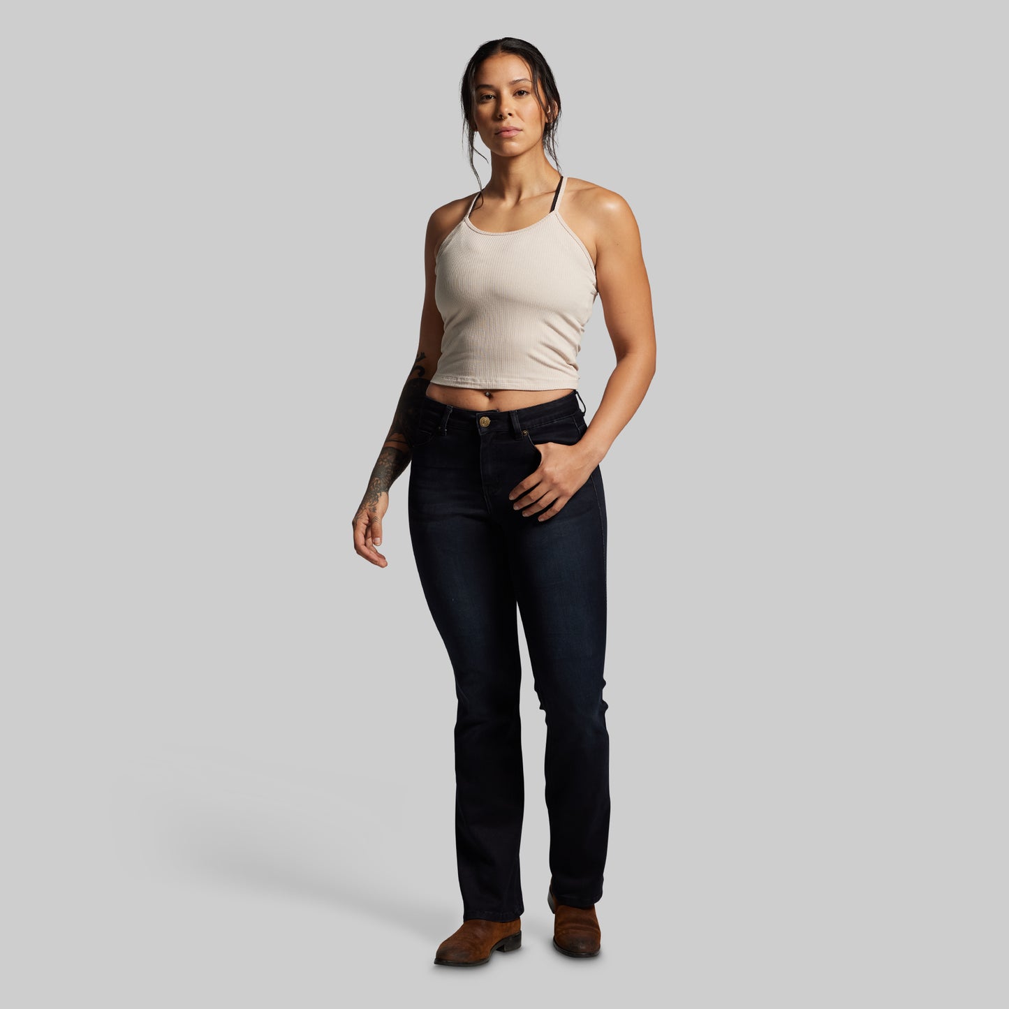 Woman wearing a beige tank top and black jeans on a gray background