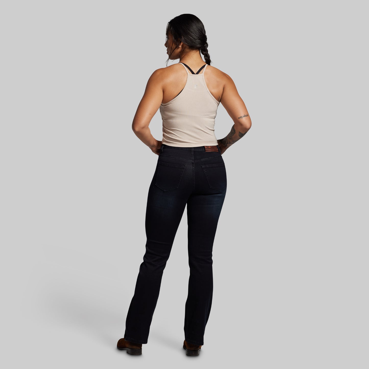 Woman wearing a beige tank top and dark jeans on a gray background