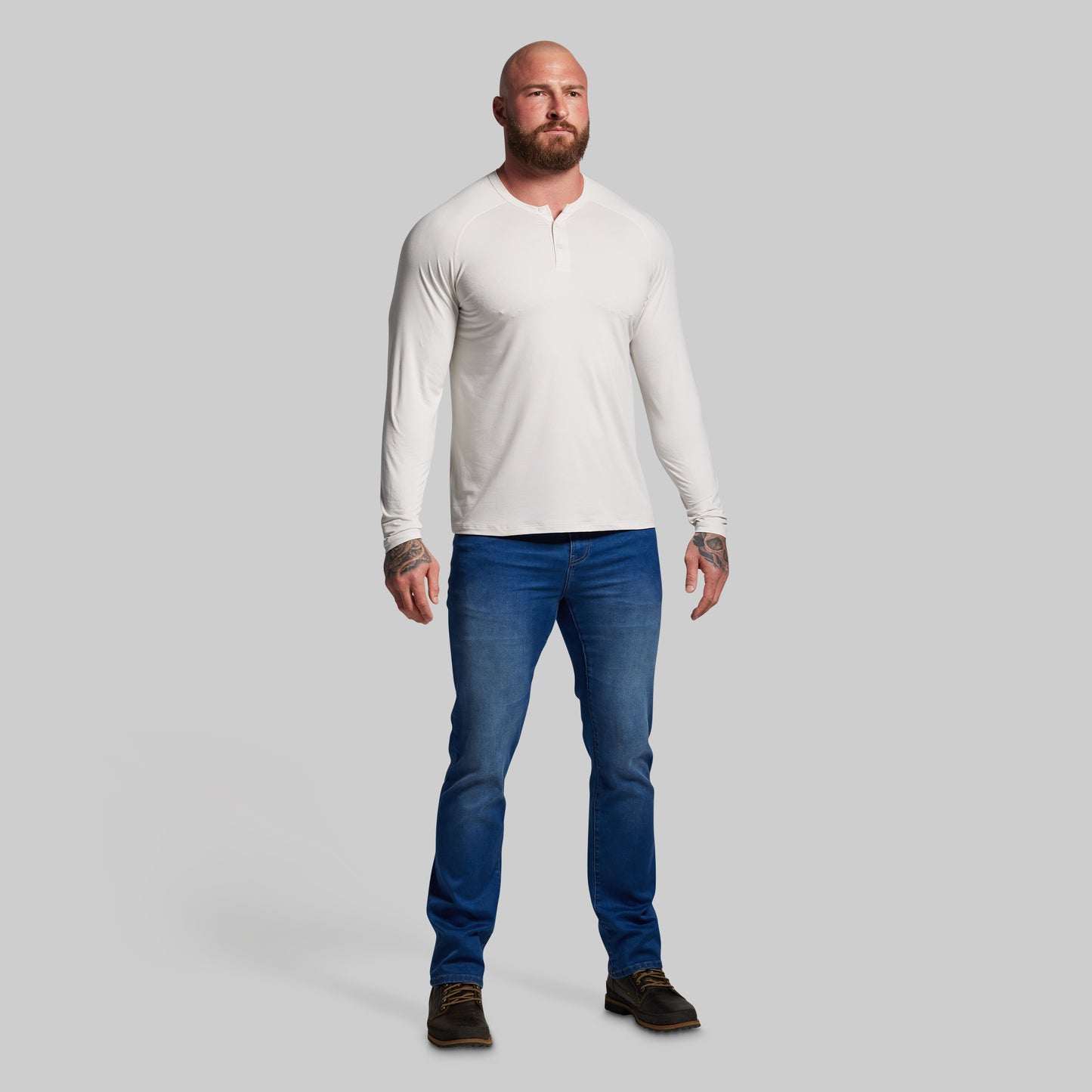 Man wearing a white long-sleeve shirt and blue jeans on a gray background