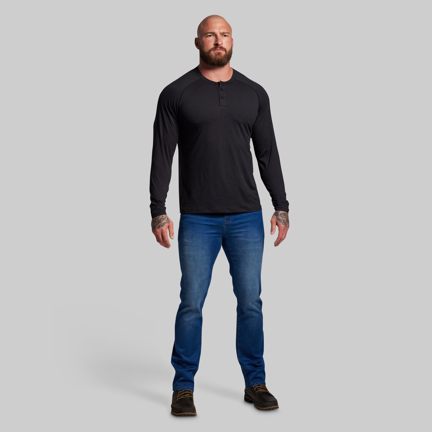Man wearing a black long-sleeve shirt and blue jeans on a gray background