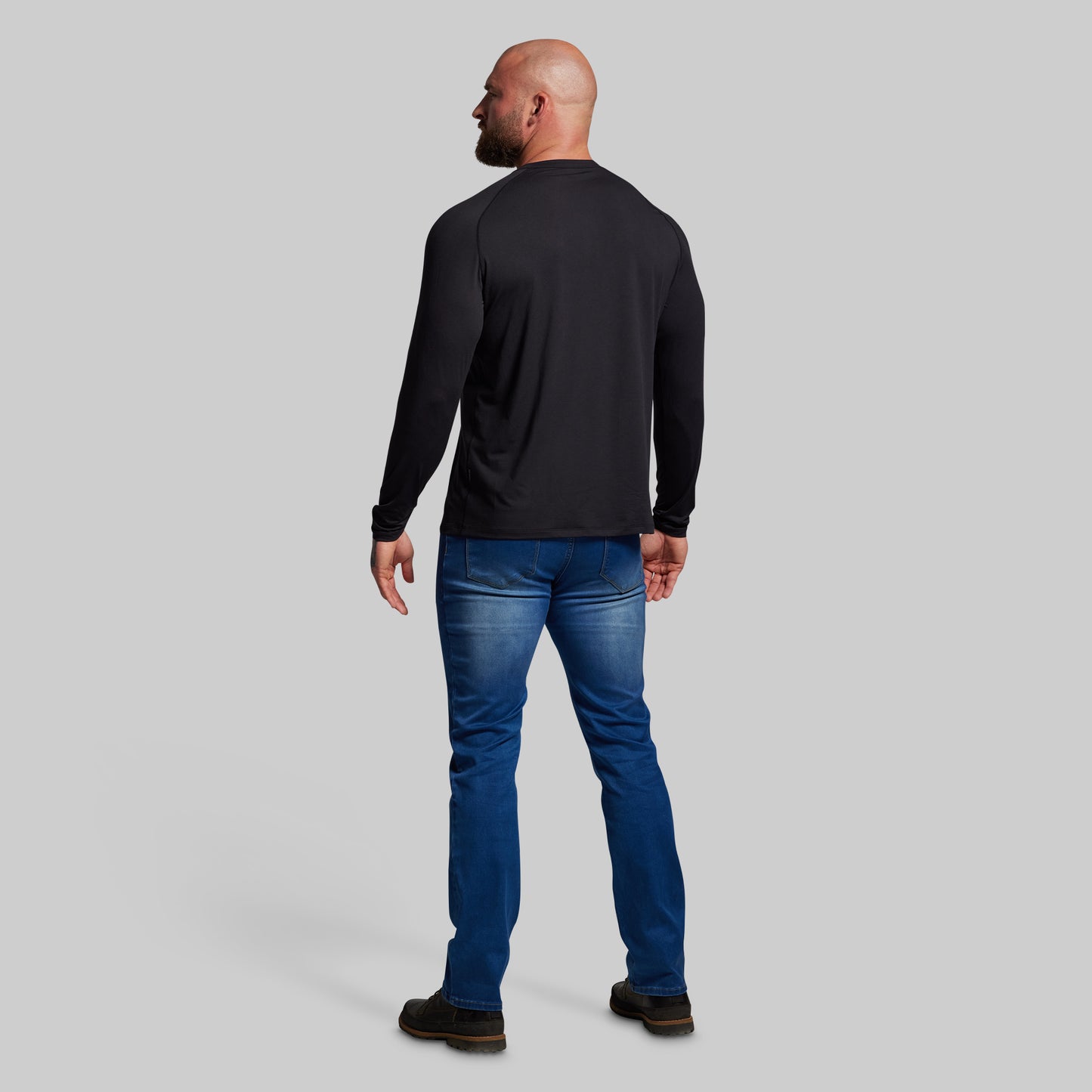 Man wearing a black long-sleeve shirt and blue jeans on a gray background
