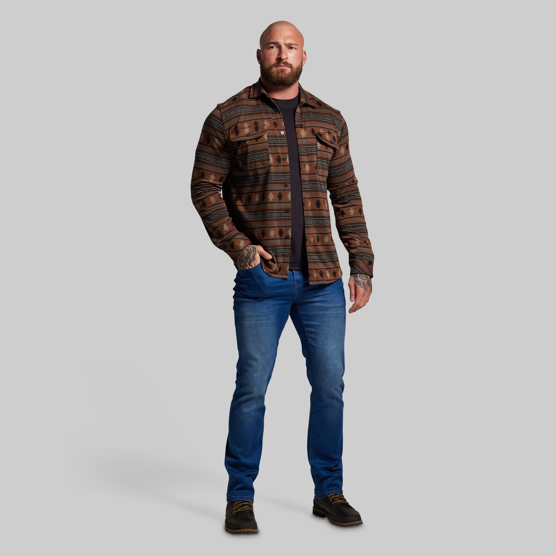 Man wearing a patterned flannel and blue jeans on a gray background