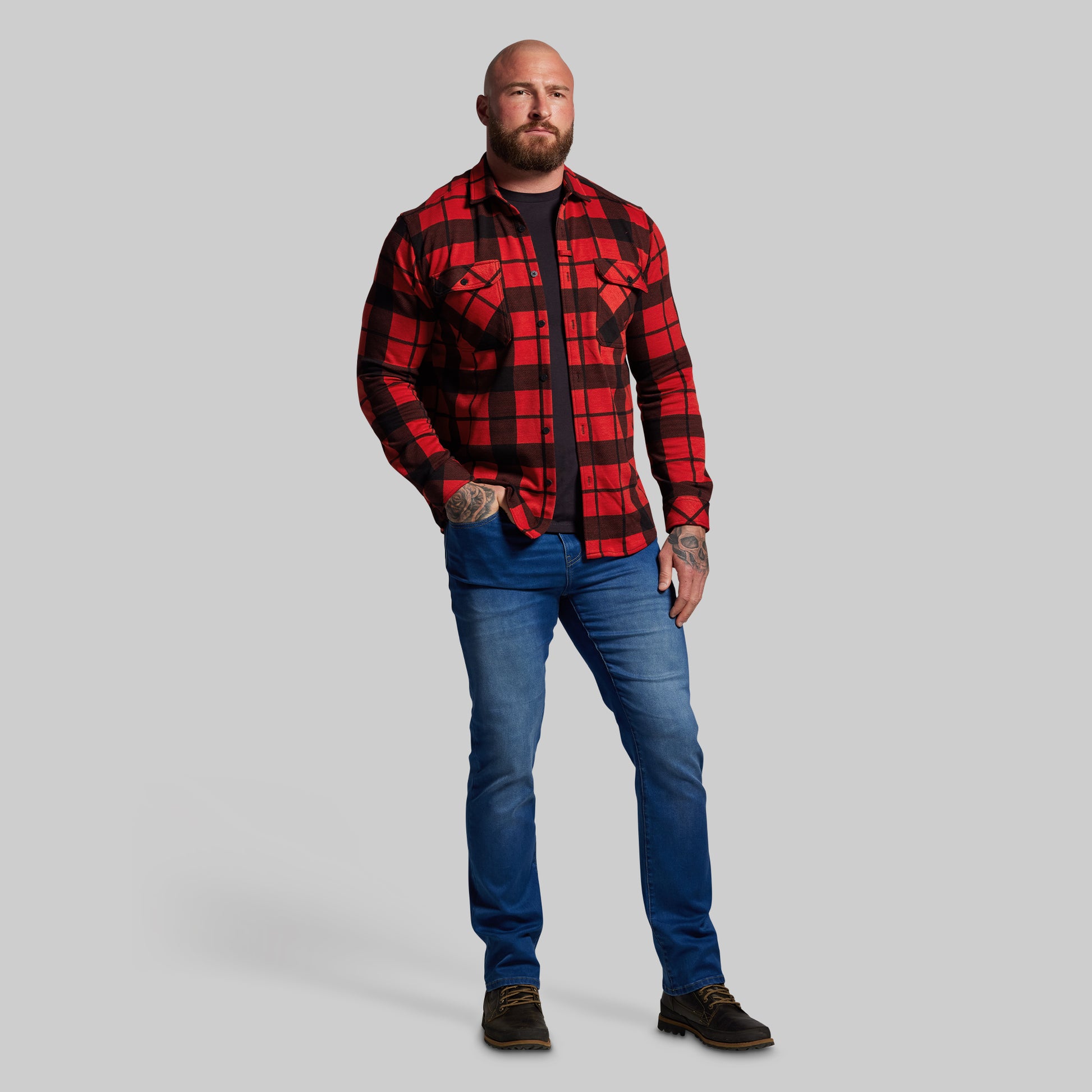 Man wearing a red and black plaid shirt and blue jeans on a gray background