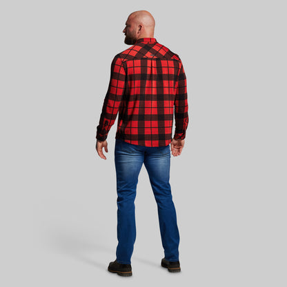 Man wearing a red and black plaid shirt and blue jeans on a gray background