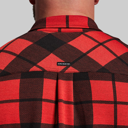 Red and black plaid shirt with 'Born Primitive' logo on a gray background