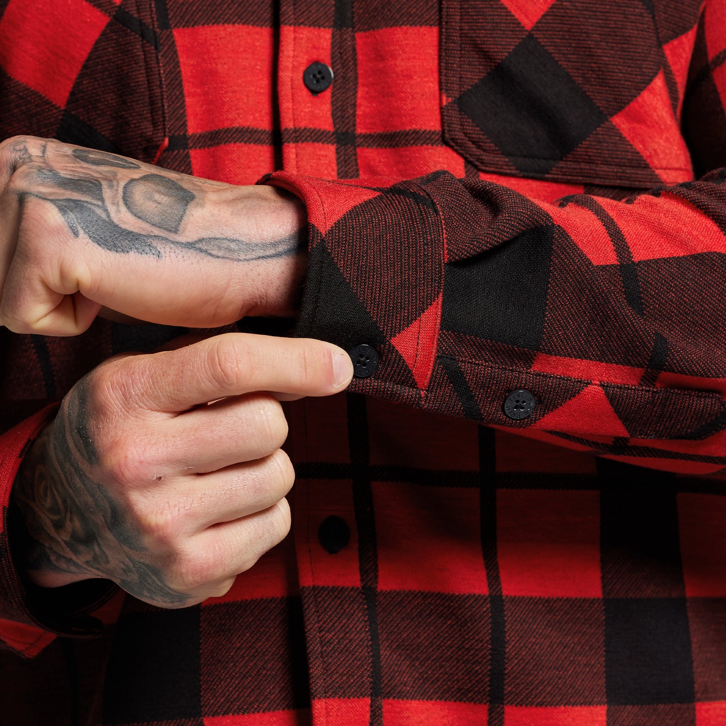 Red and black plaid shirt with a close-up of a hand adjusting the cuff.
