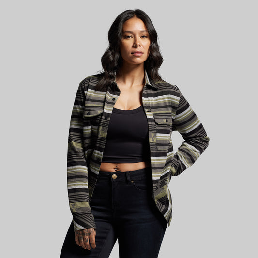 Woman wearing a patterned shirt over a black top and jeans on a gray background