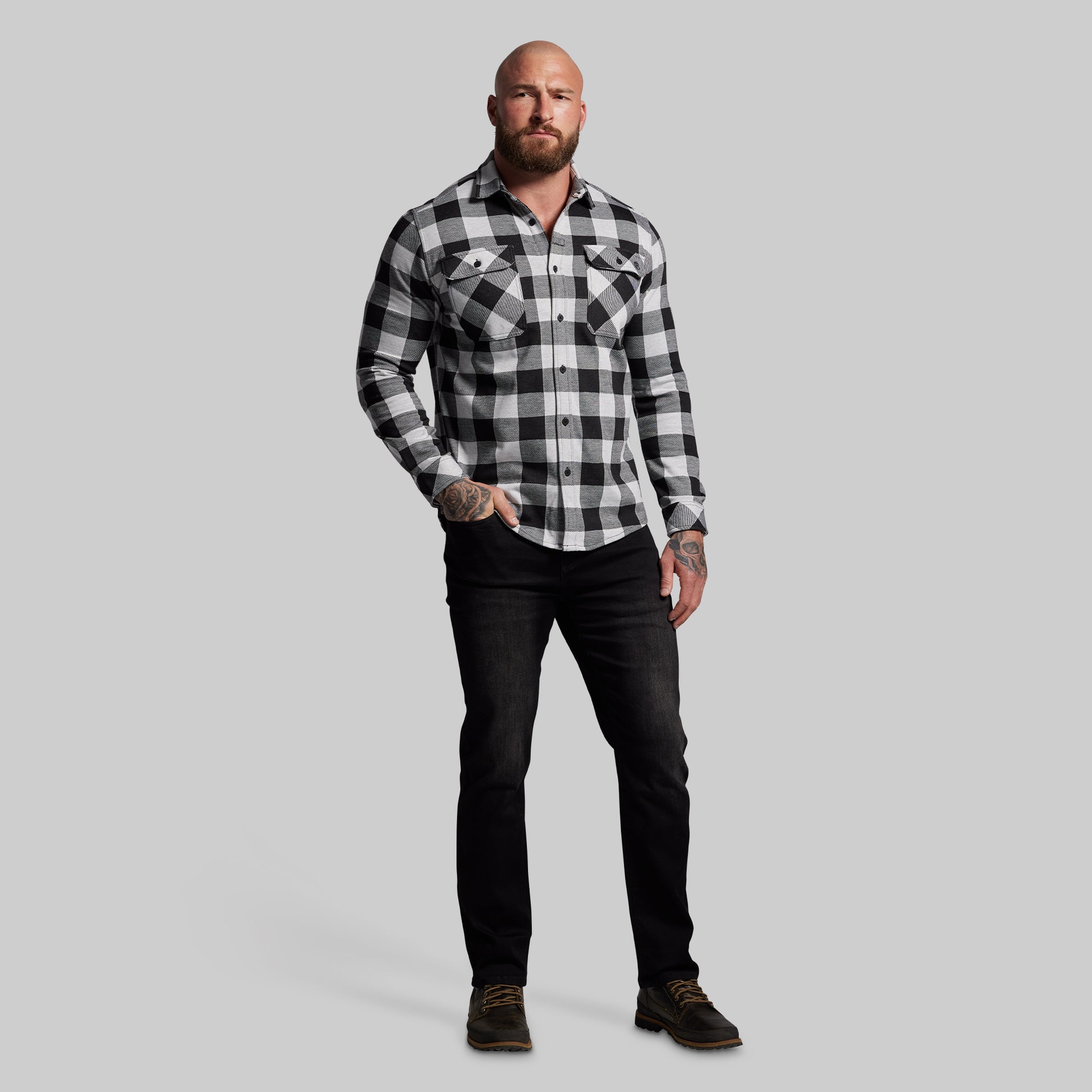 Man wearing a black and white checkered shirt and black pants on a gray background