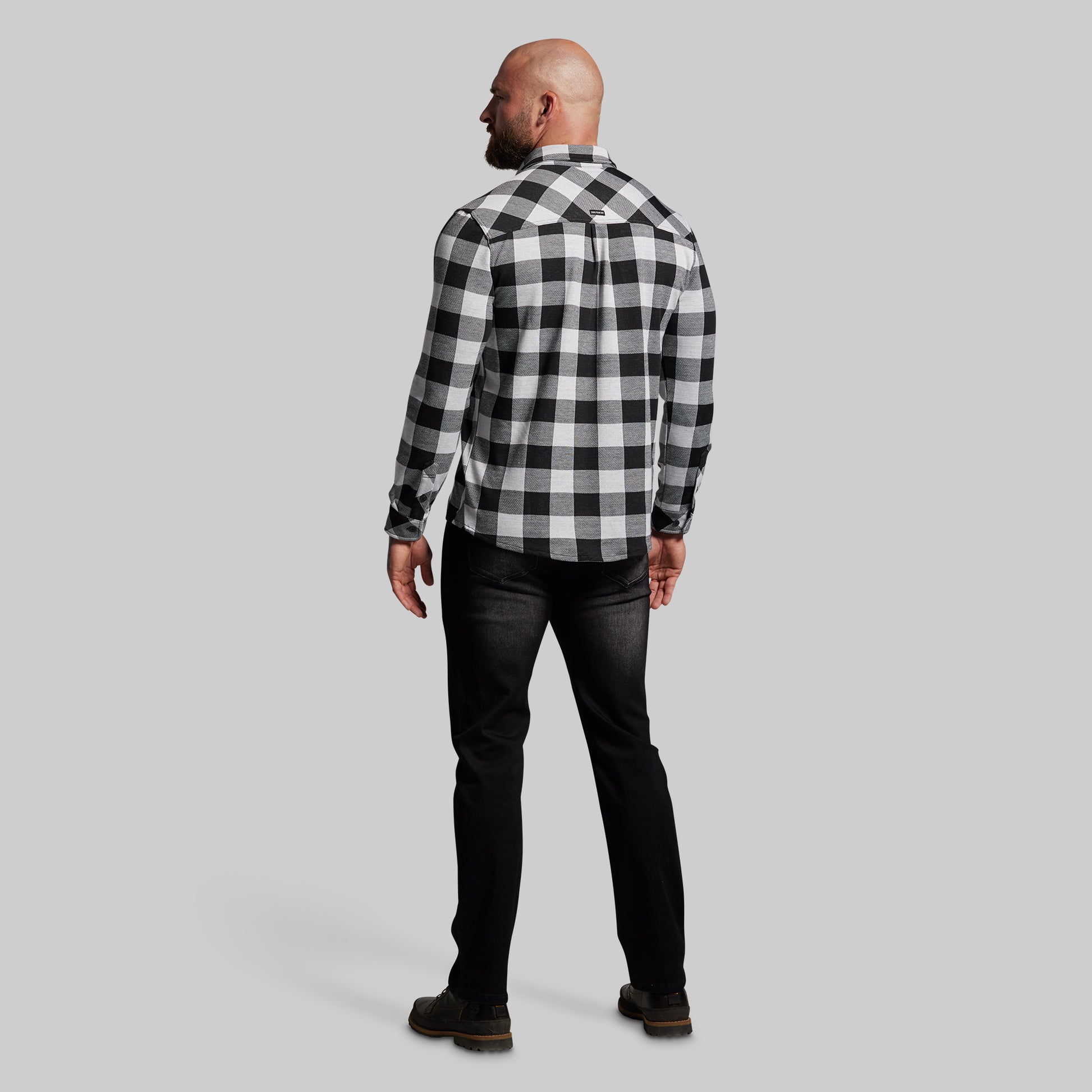 Man wearing a black and white checkered shirt and dark jeans on a gray background
