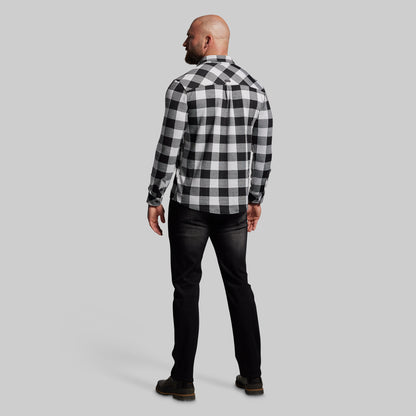 Man wearing a black and white checkered shirt and dark jeans on a gray background