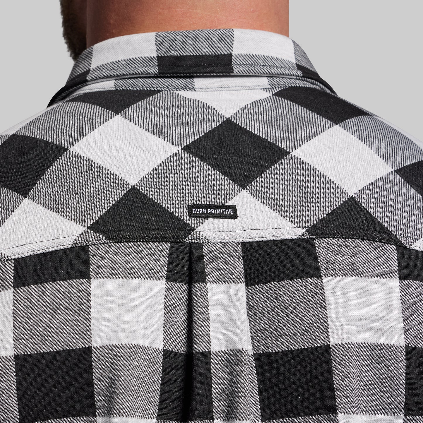 Black and white checkered shirt with 'Born Primitive' logo on a gray background