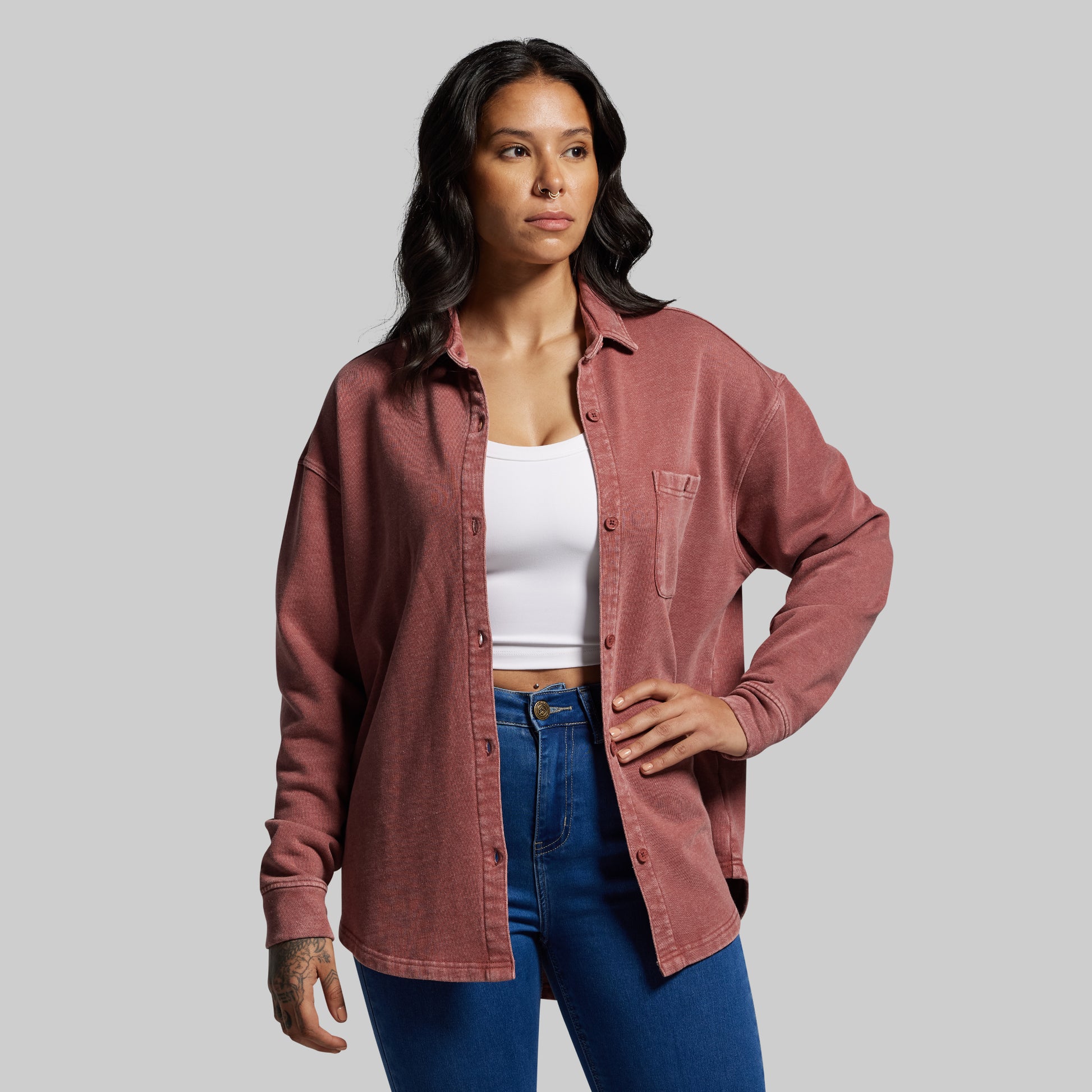 Woman wearing a pink shirt over a white top and blue jeans on a gray background