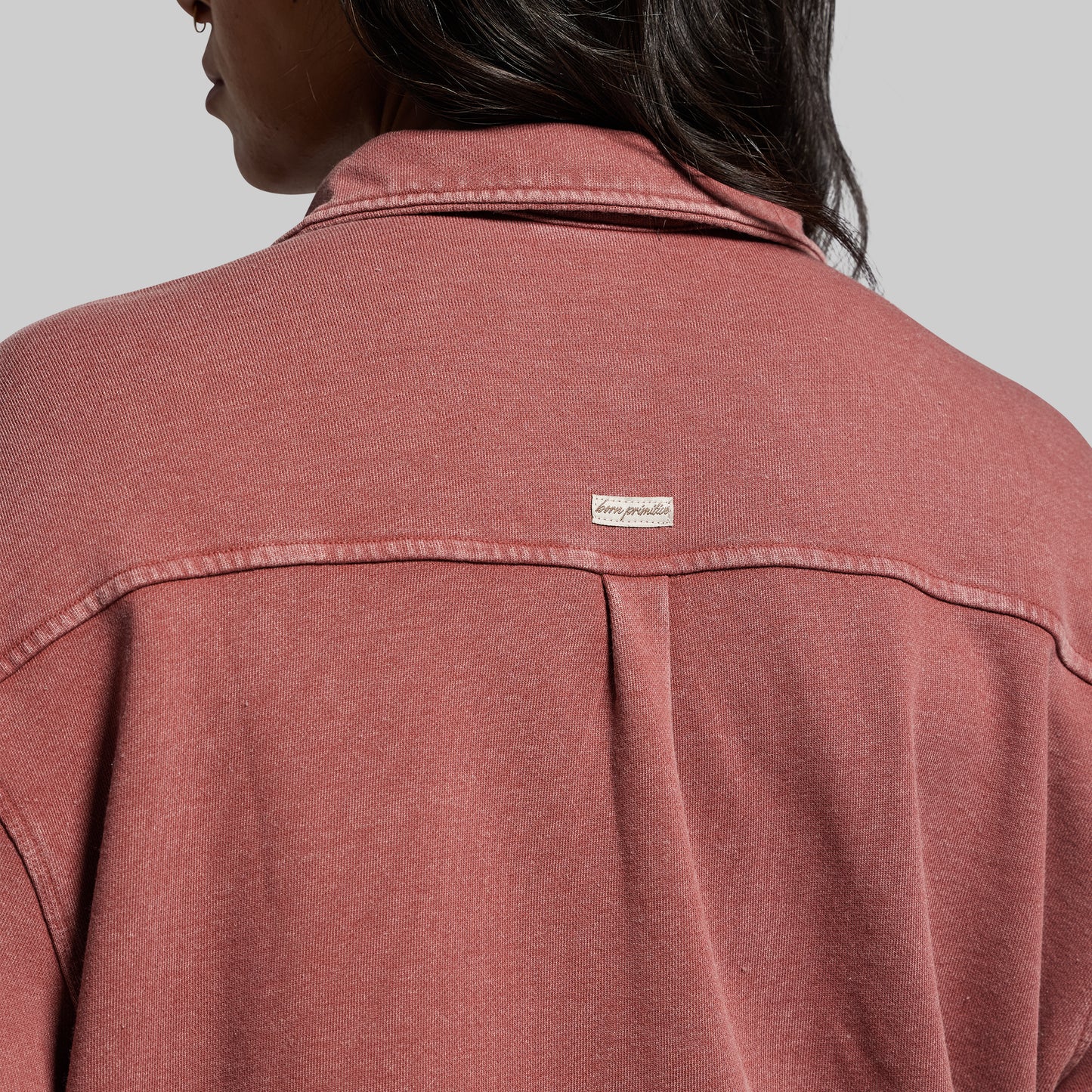 Close-up of a person wearing a red shirt with a brand label on a gray background