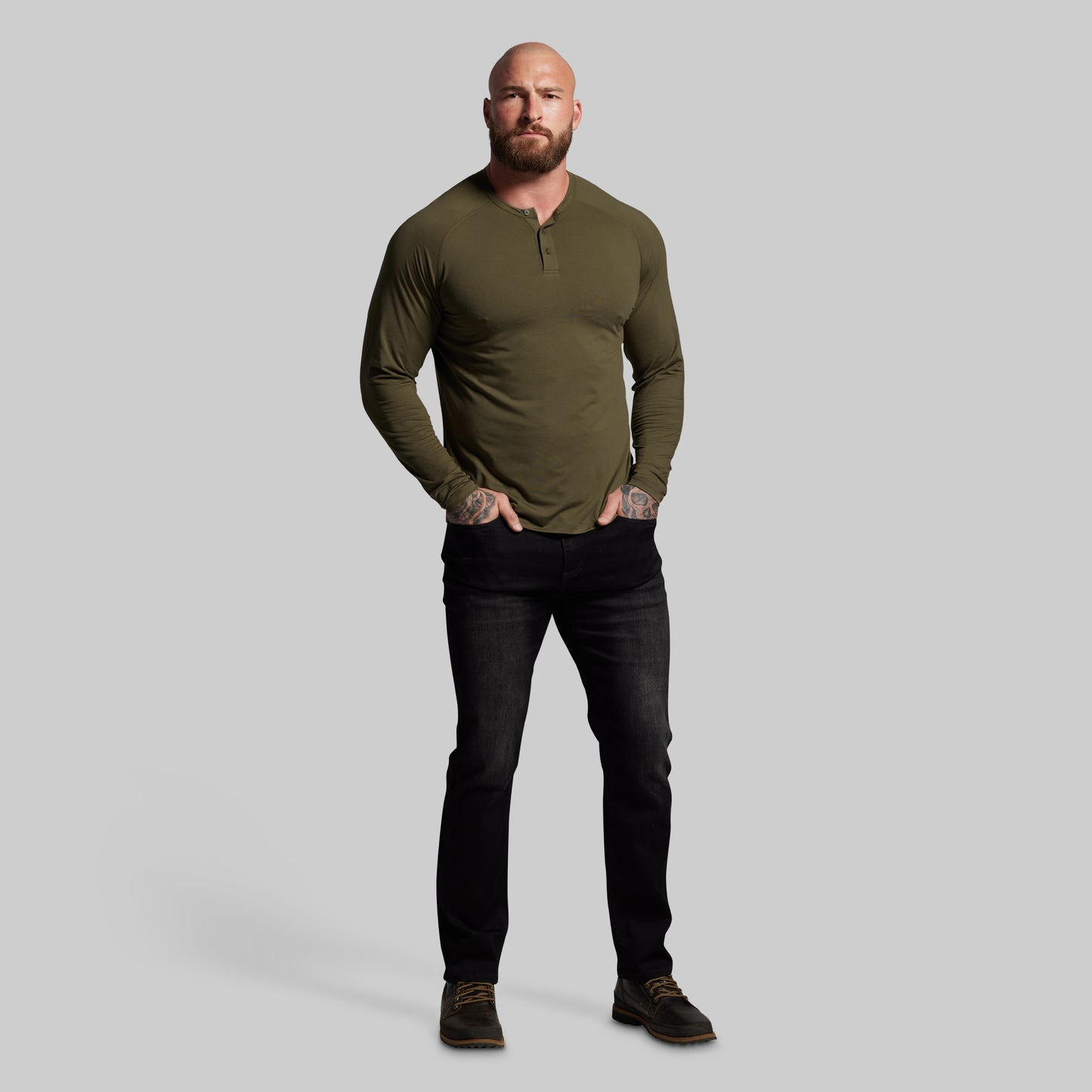 Man wearing an olive green long-sleeve shirt and black jeans on a gray background