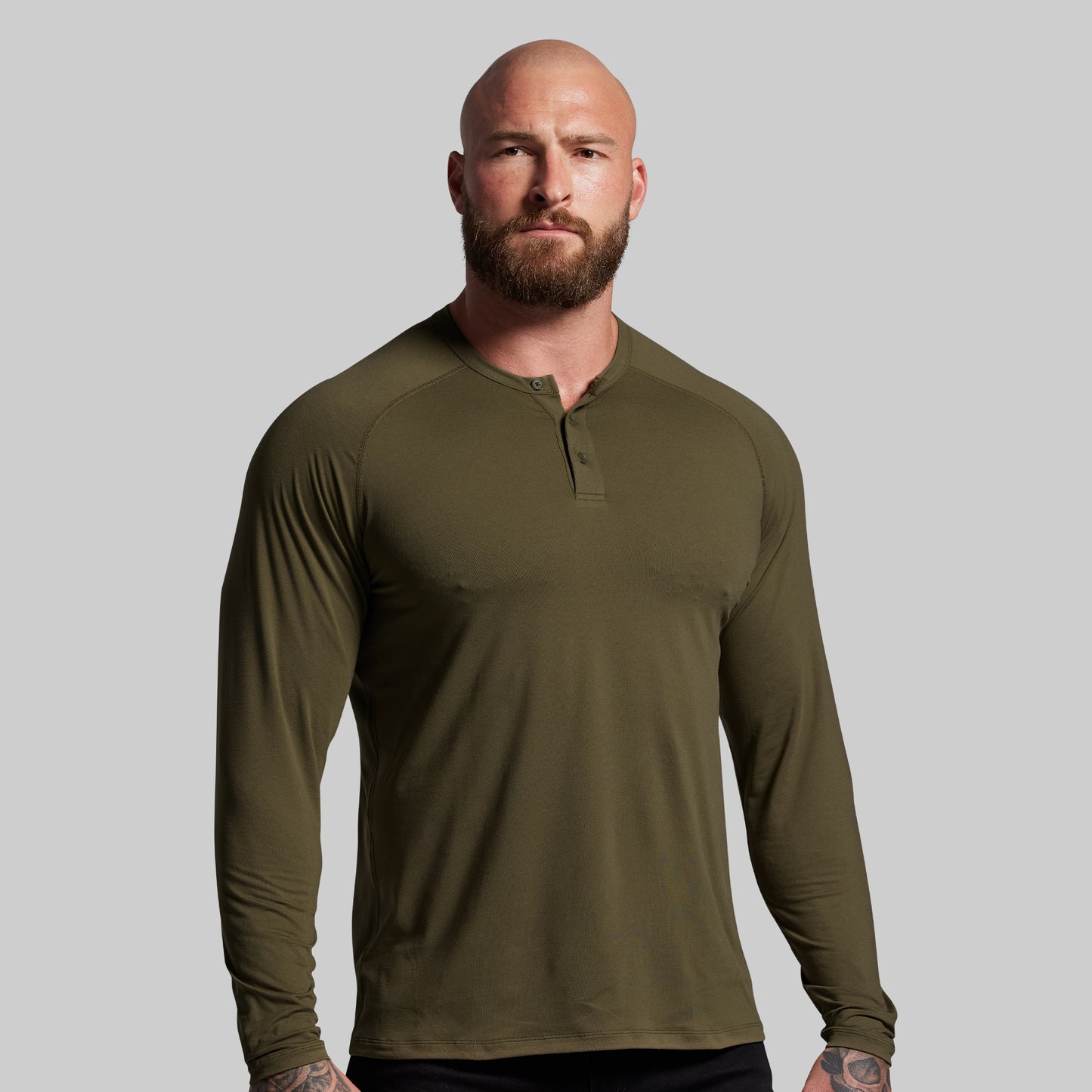 Man wearing an olive green long-sleeve shirt against a gray background