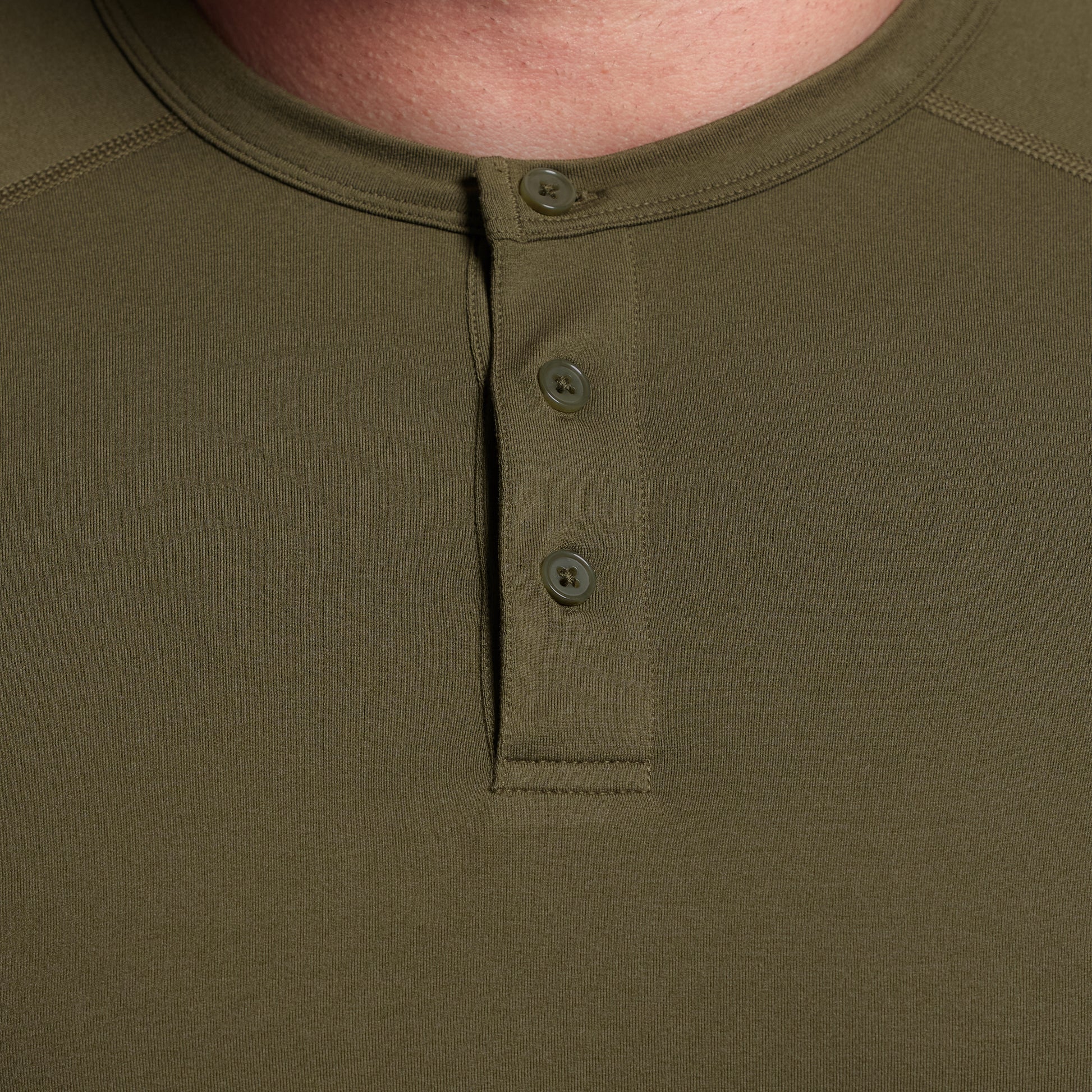 Close-up of a green henley shirt with buttons on a plain background