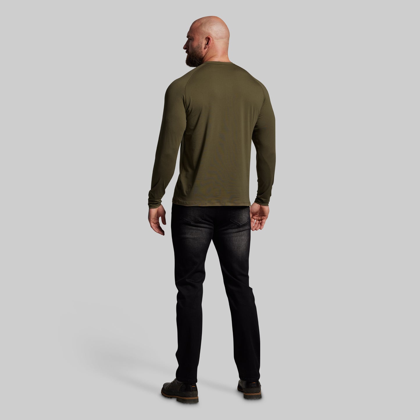 Man wearing an olive green long-sleeve shirt and black pants on a gray background