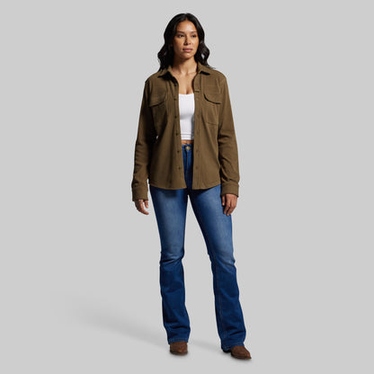 Woman wearing a brown button up and blue jeans on a gray background