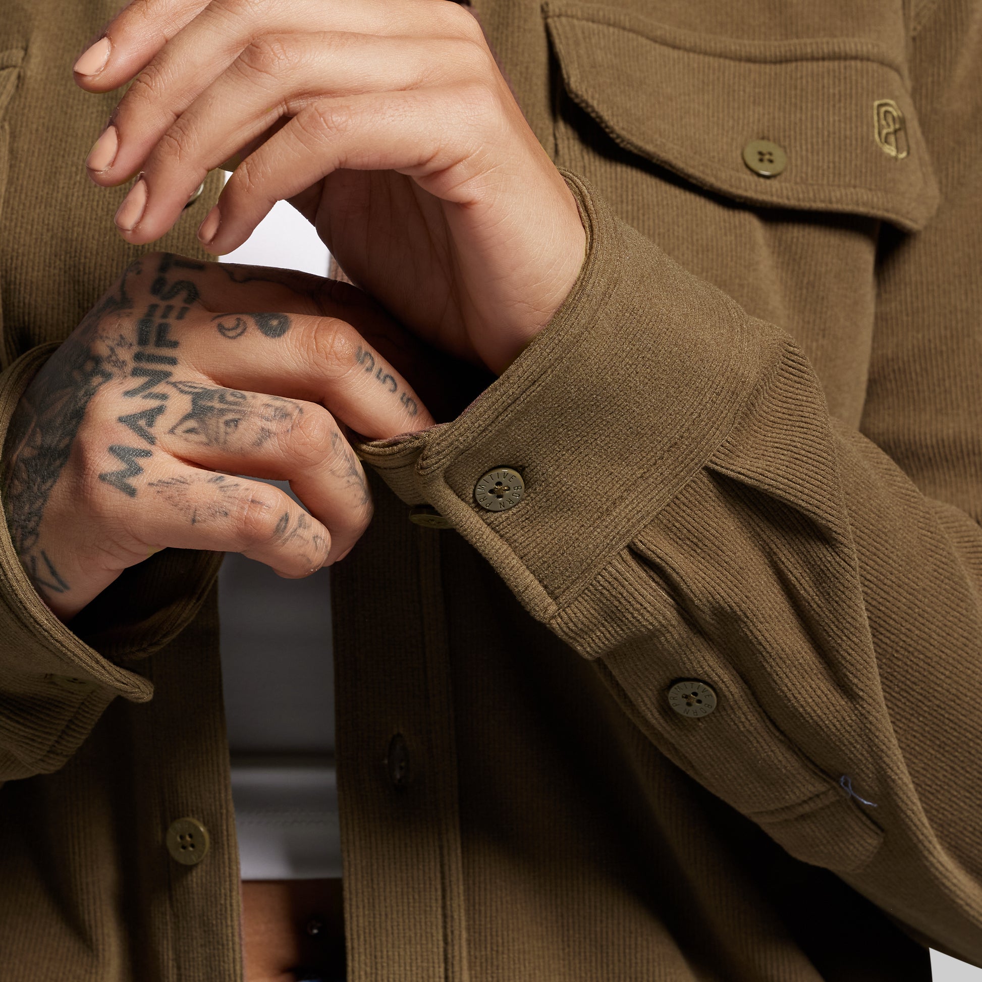 Close-up of a person wearing a brown long sleeve with visible tattoos on their hands.