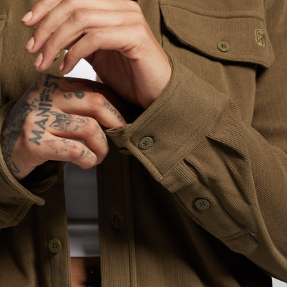 Close-up of a person wearing a brown long sleeve with visible tattoos on their hands.