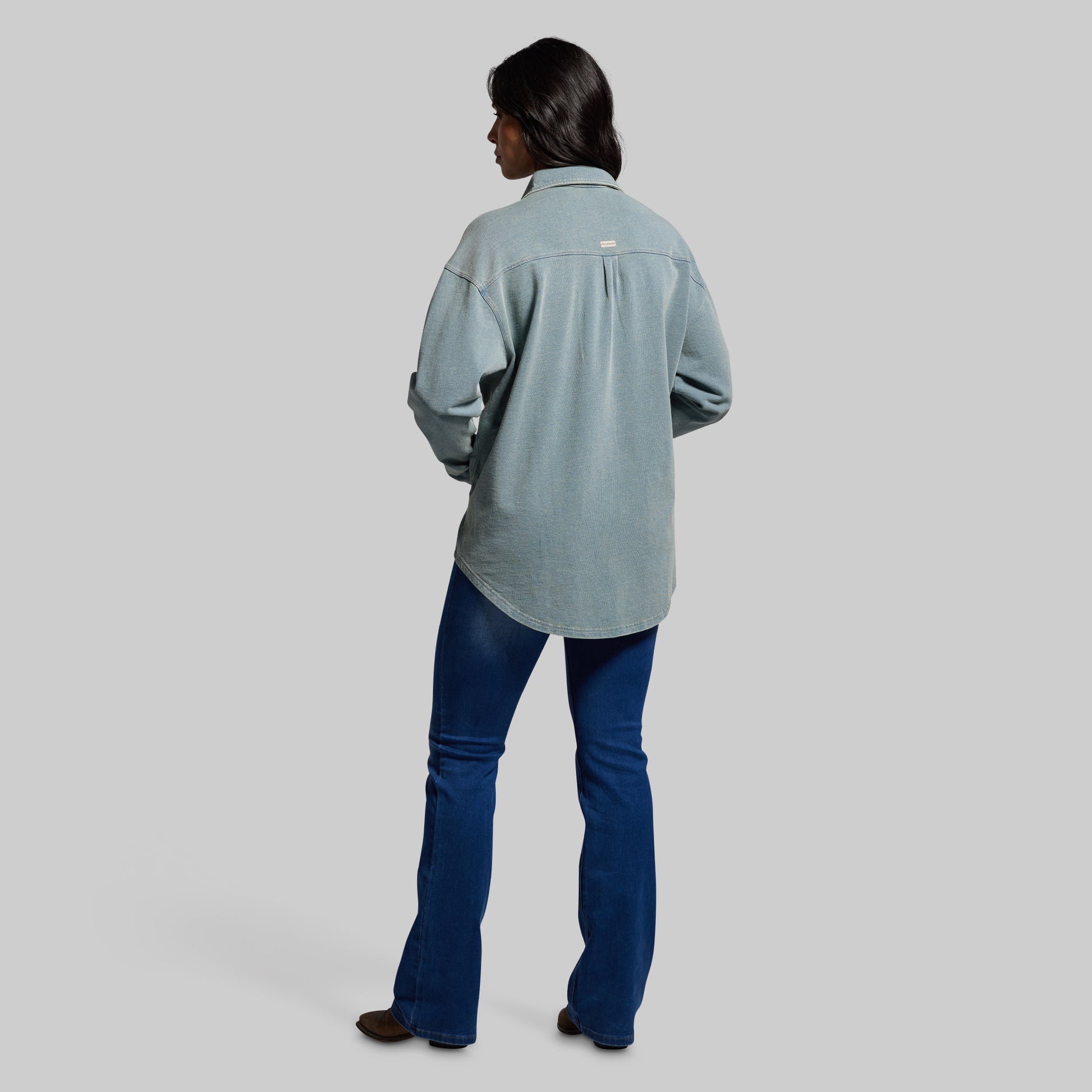 Person wearing a light blue shirt and blue jeans on a gray background