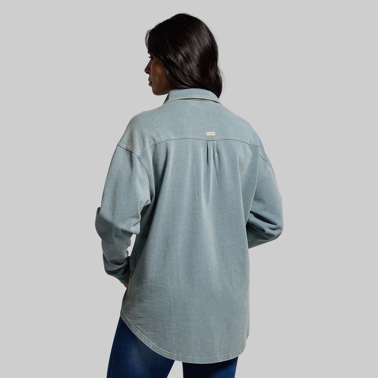 Person wearing a light blue denim shirt on a gray background