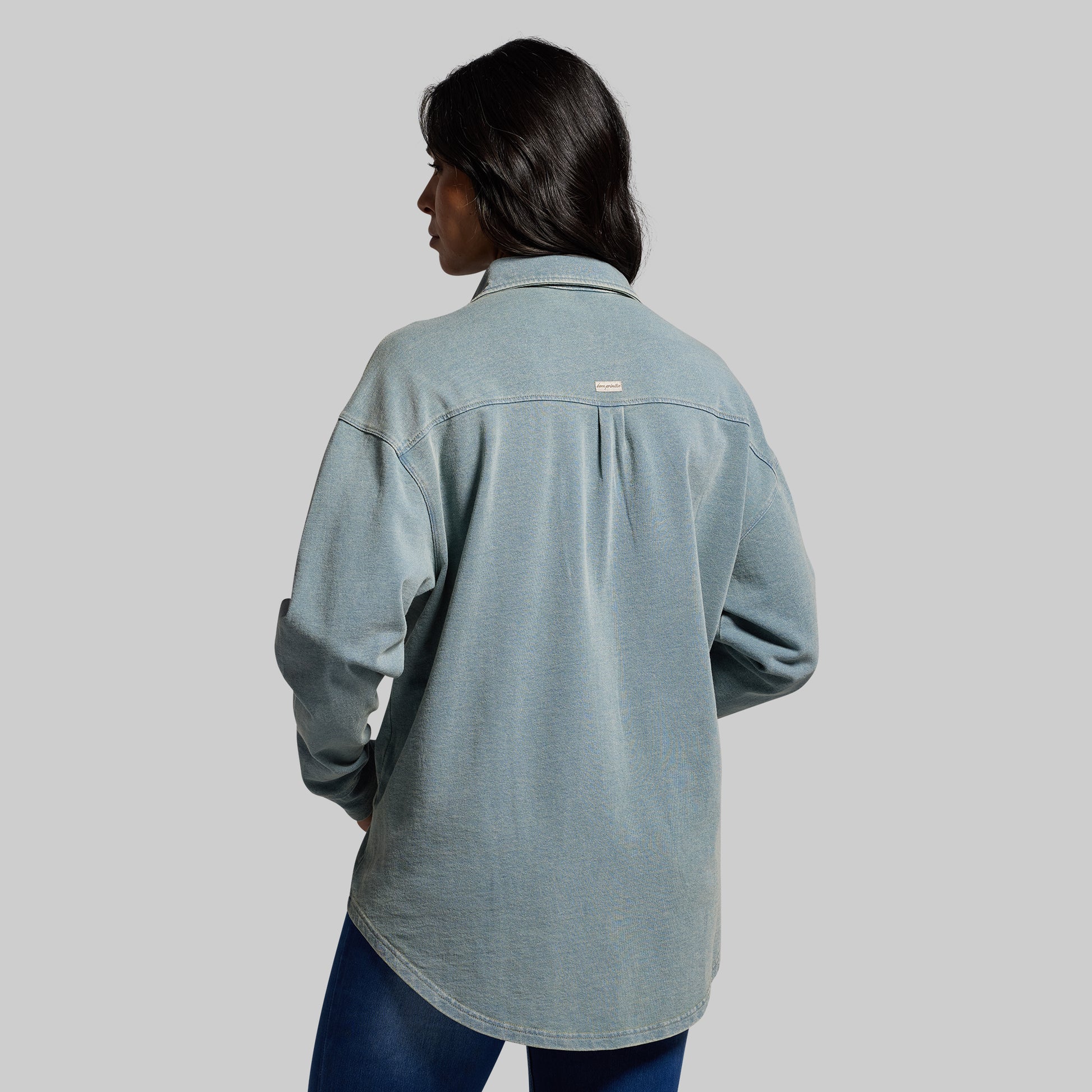 Person wearing a light blue denim shirt on a gray background