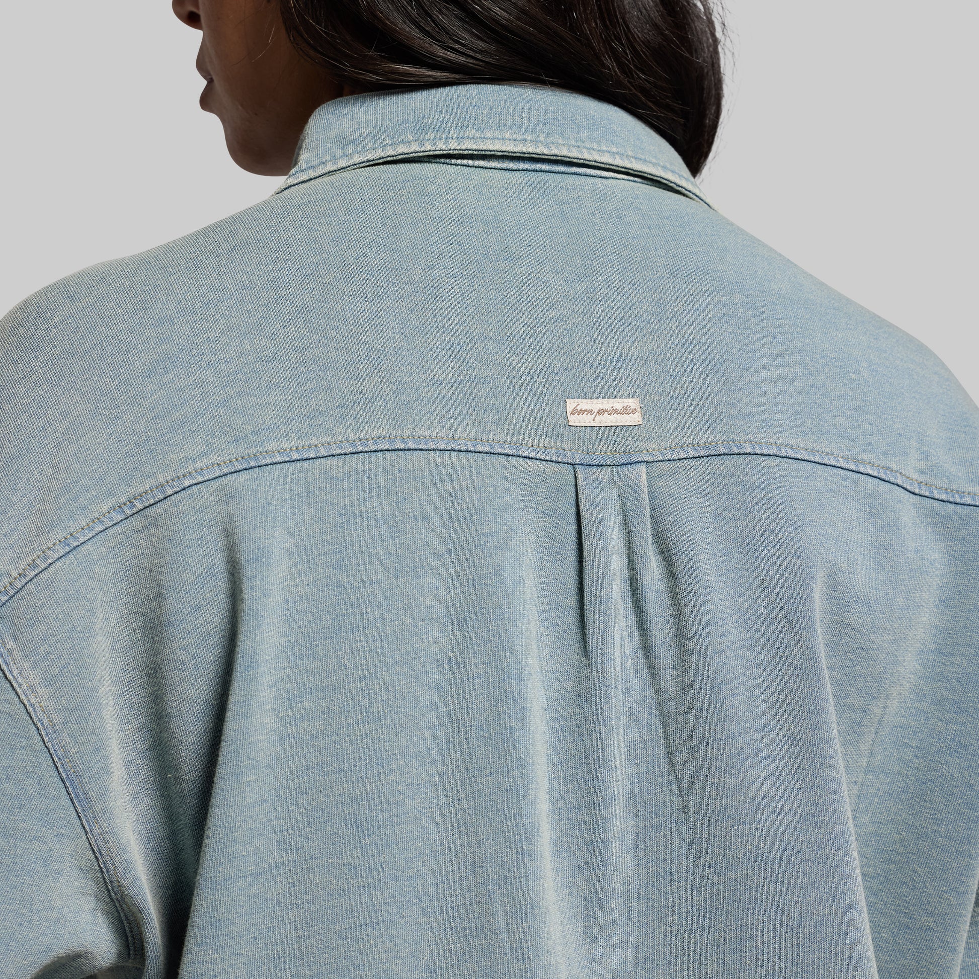 Light blue denim shirt with a brand logo on a gray background
