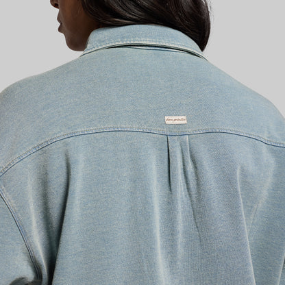 Light blue denim shirt with a brand logo on a gray background