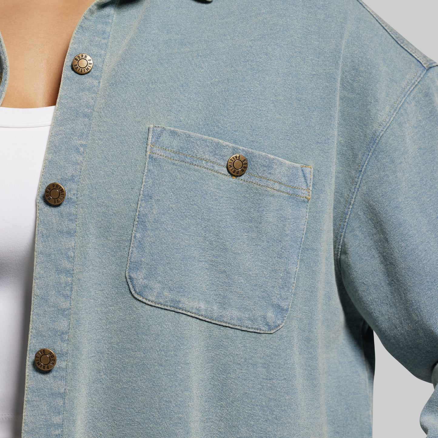 Close-up of a light blue denim shirt with button details on a neutral background