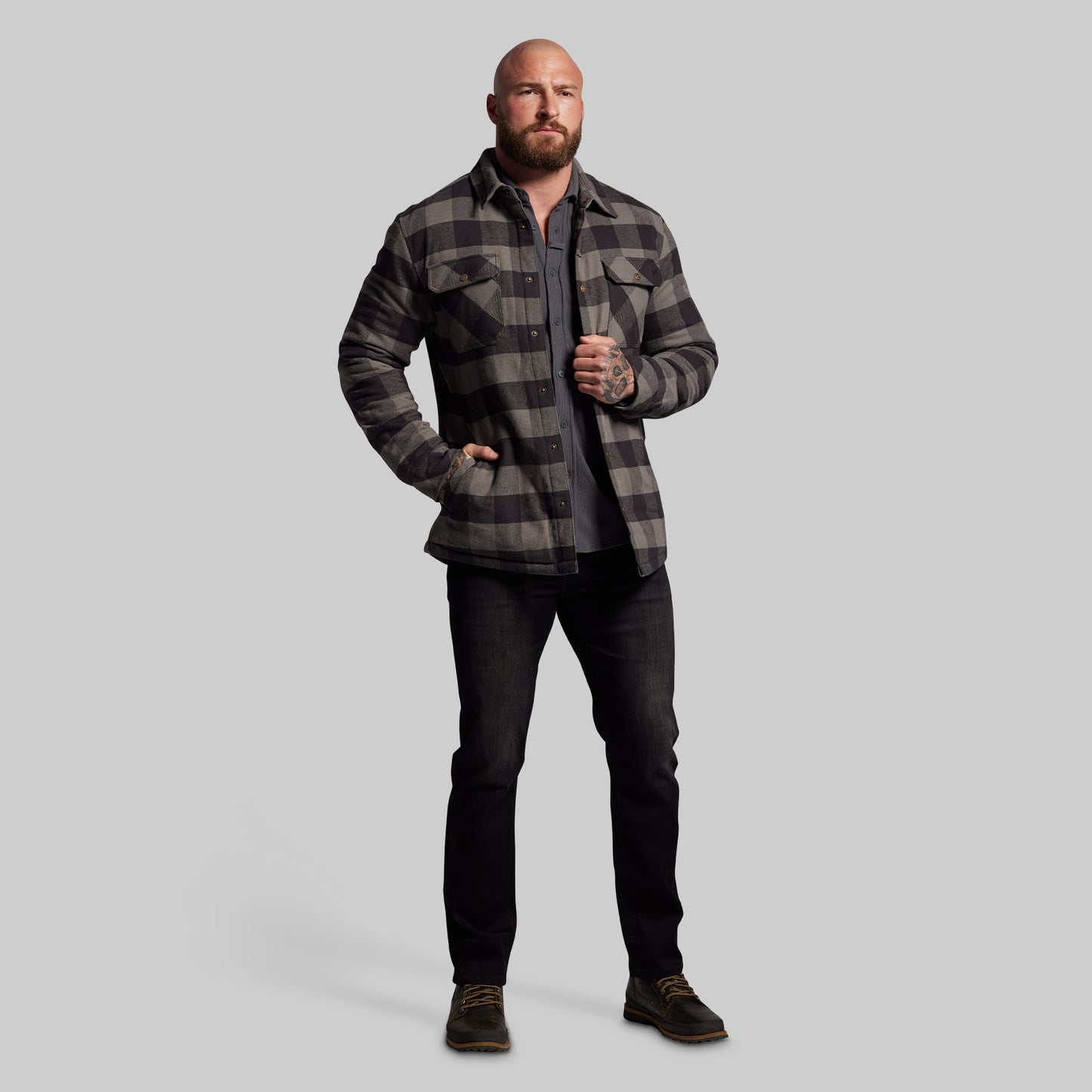 Man wearing a plaid jacket and dark jeans on a gray background