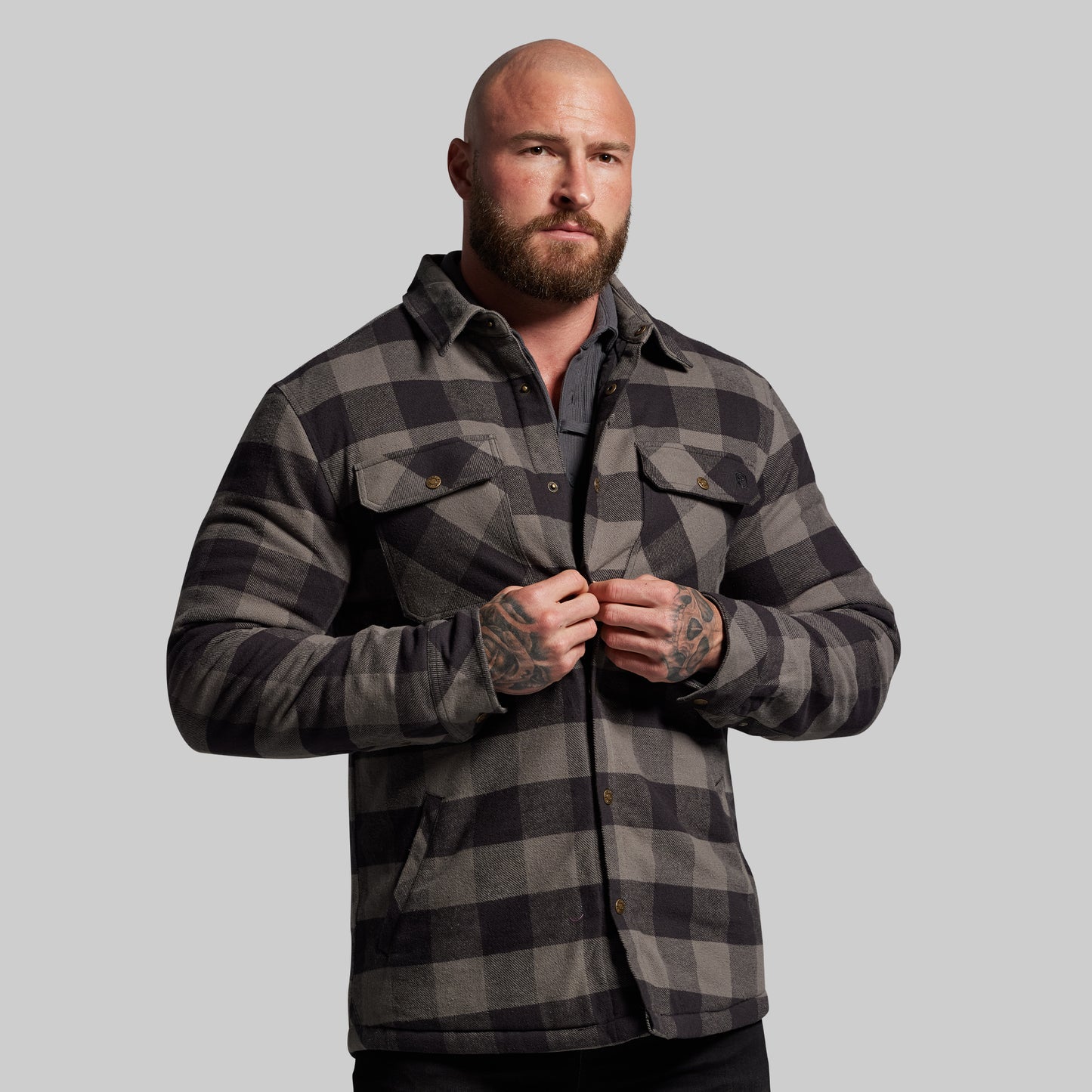 Man wearing a gray and black plaid jacket against a plain background