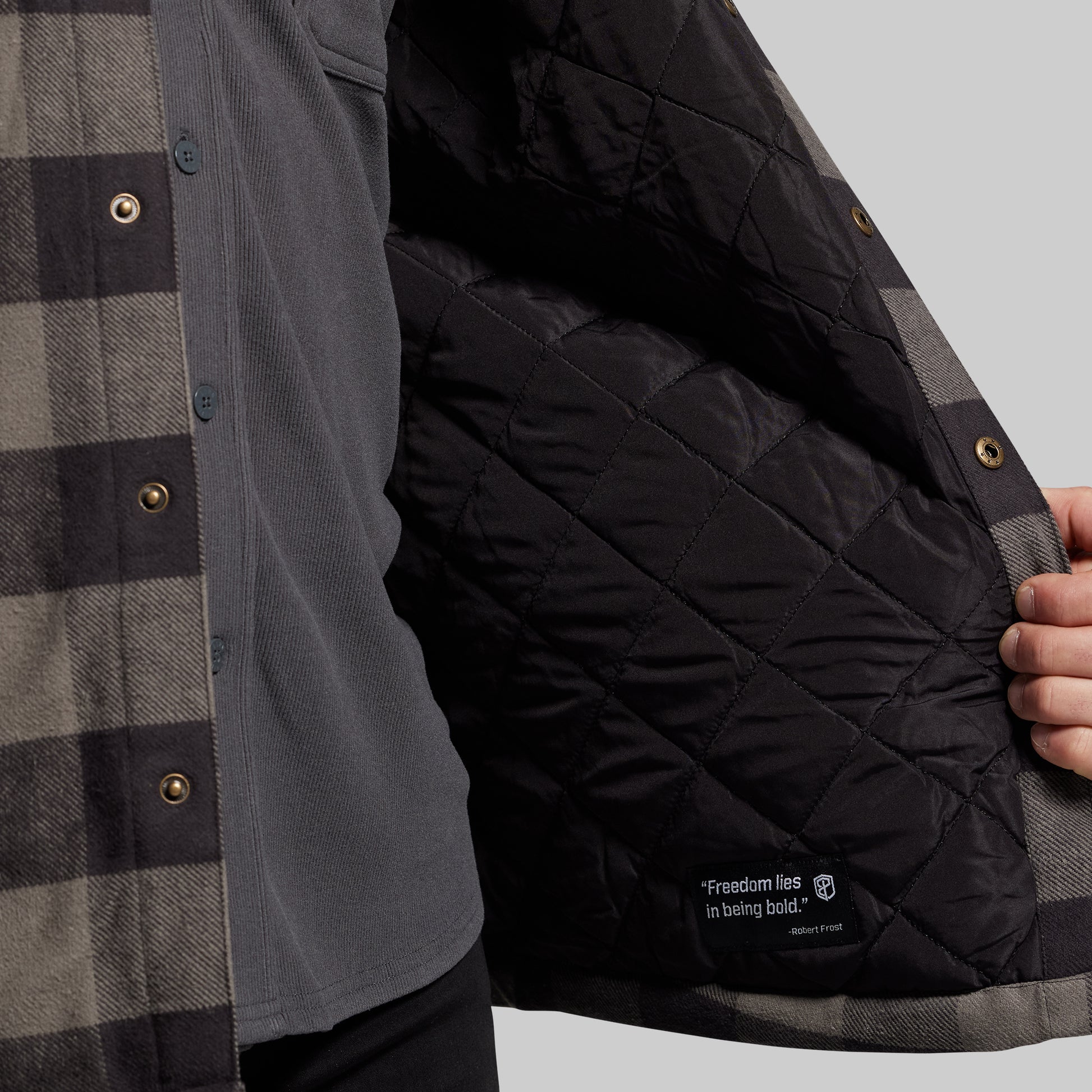 Person wearing a black quilted jacket with a textured shirt underneath, on a gray background.
