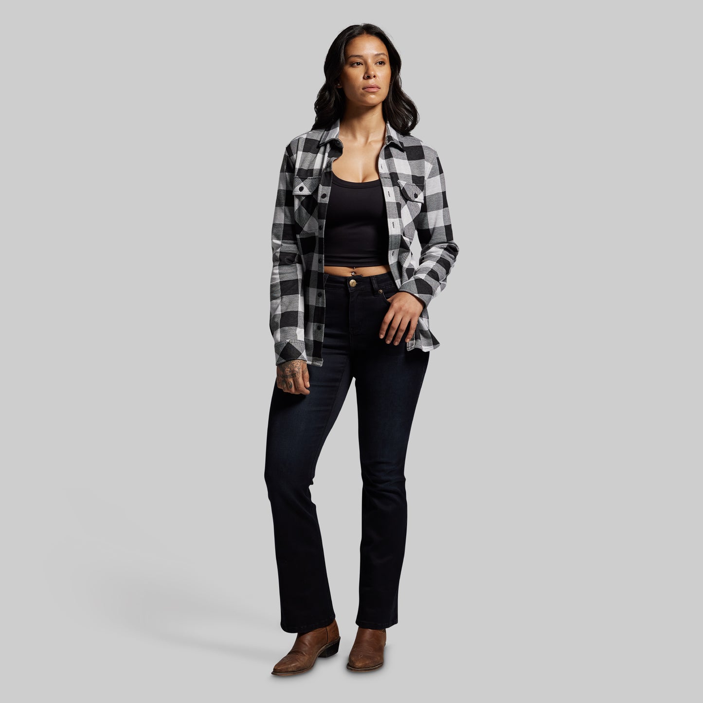 Woman wearing a plaid shirt, black top, and jeans on a gray background