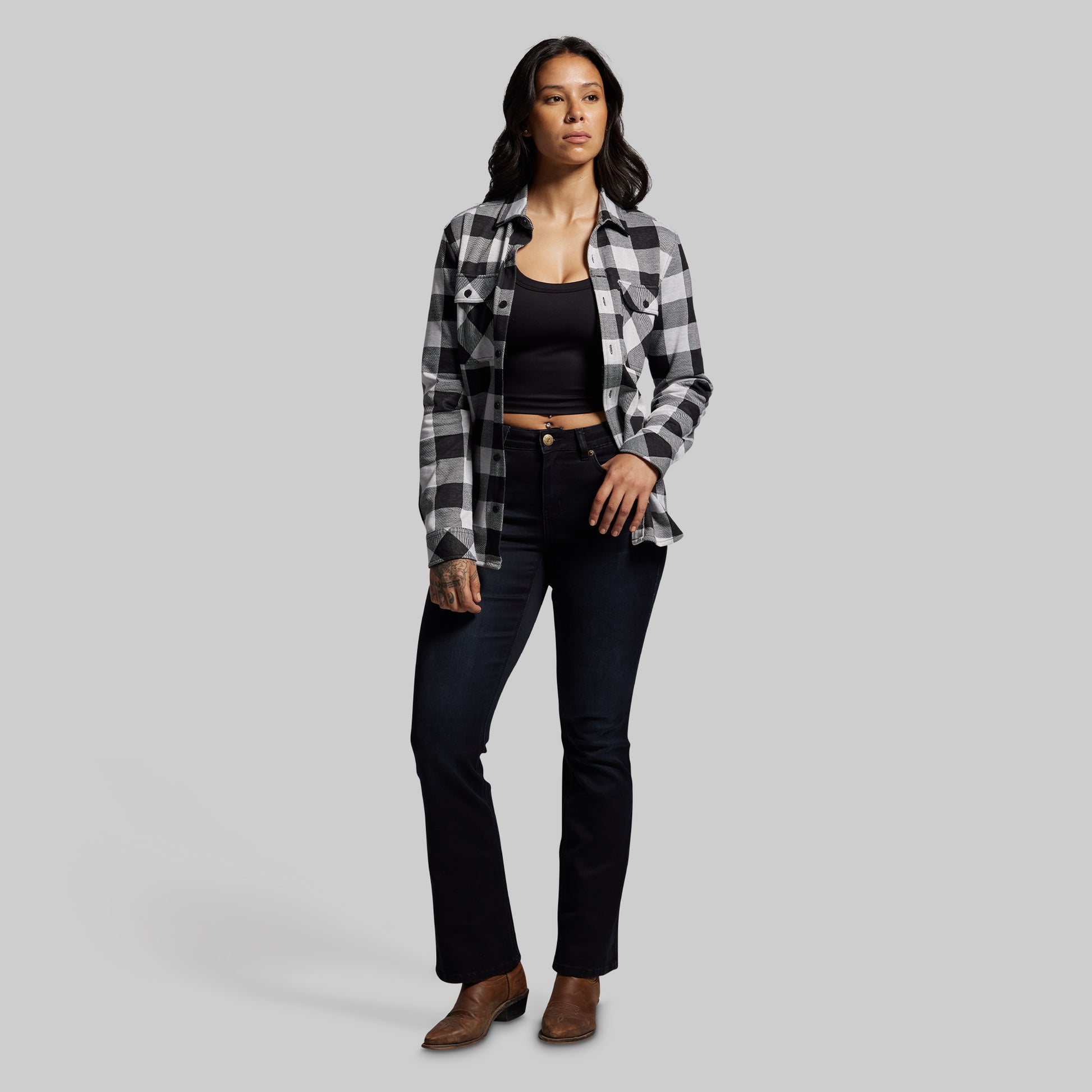 Woman wearing a plaid shirt, black top, and jeans on a gray background