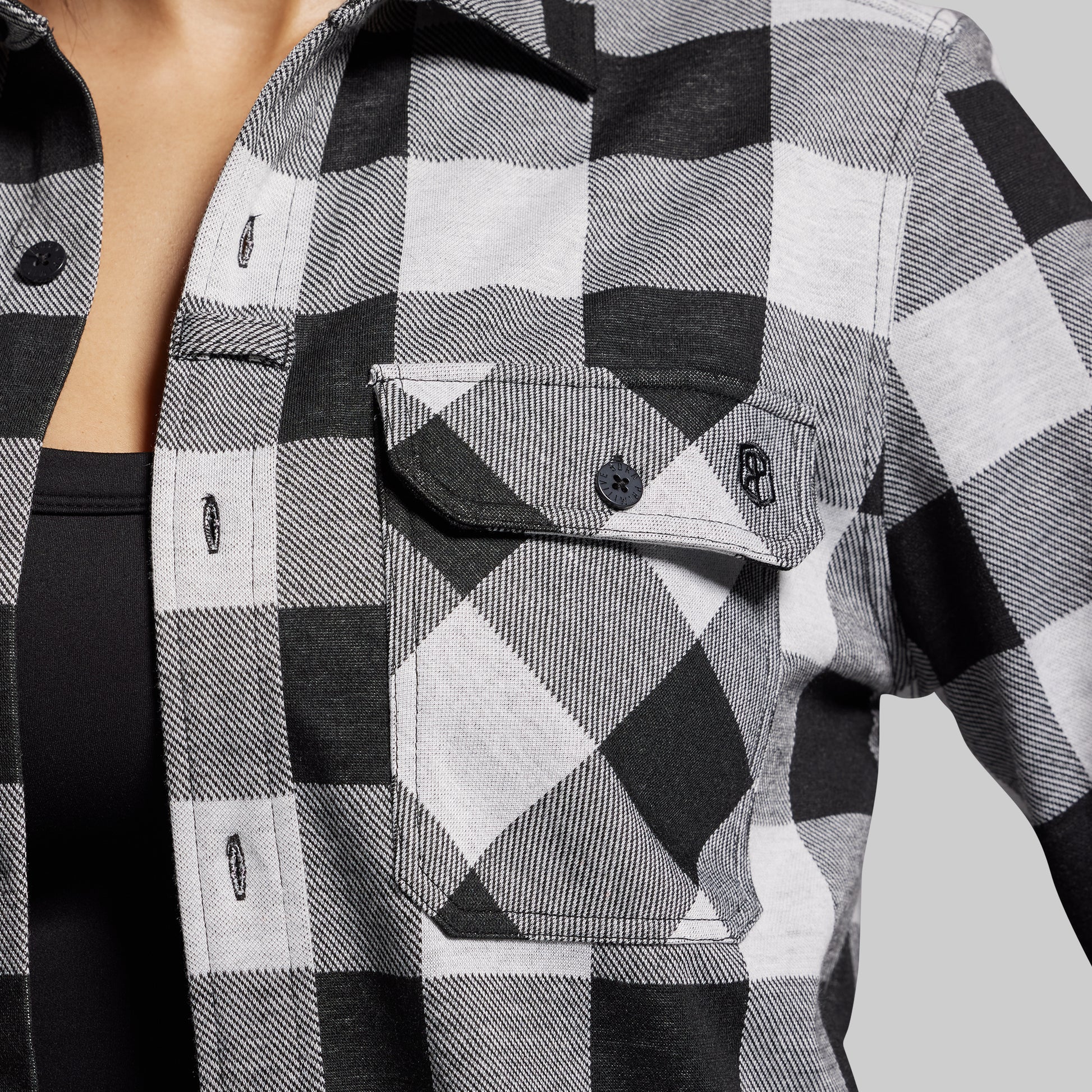 Close-up of a black and white checkered shirt with a brand logo on a gray background