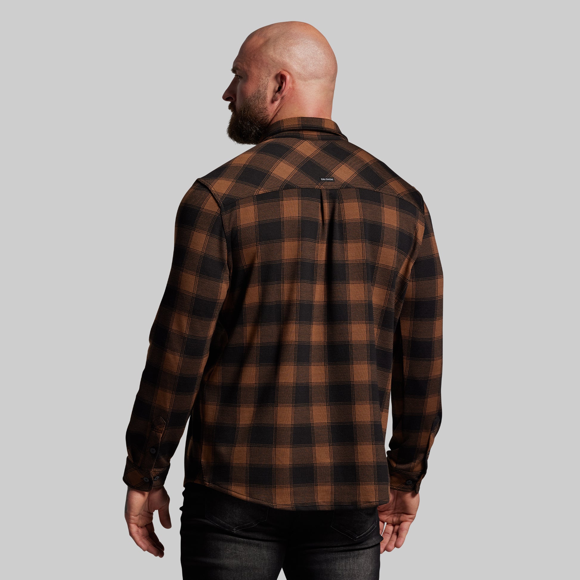 Man wearing a brown and black plaid shirt against a gray background