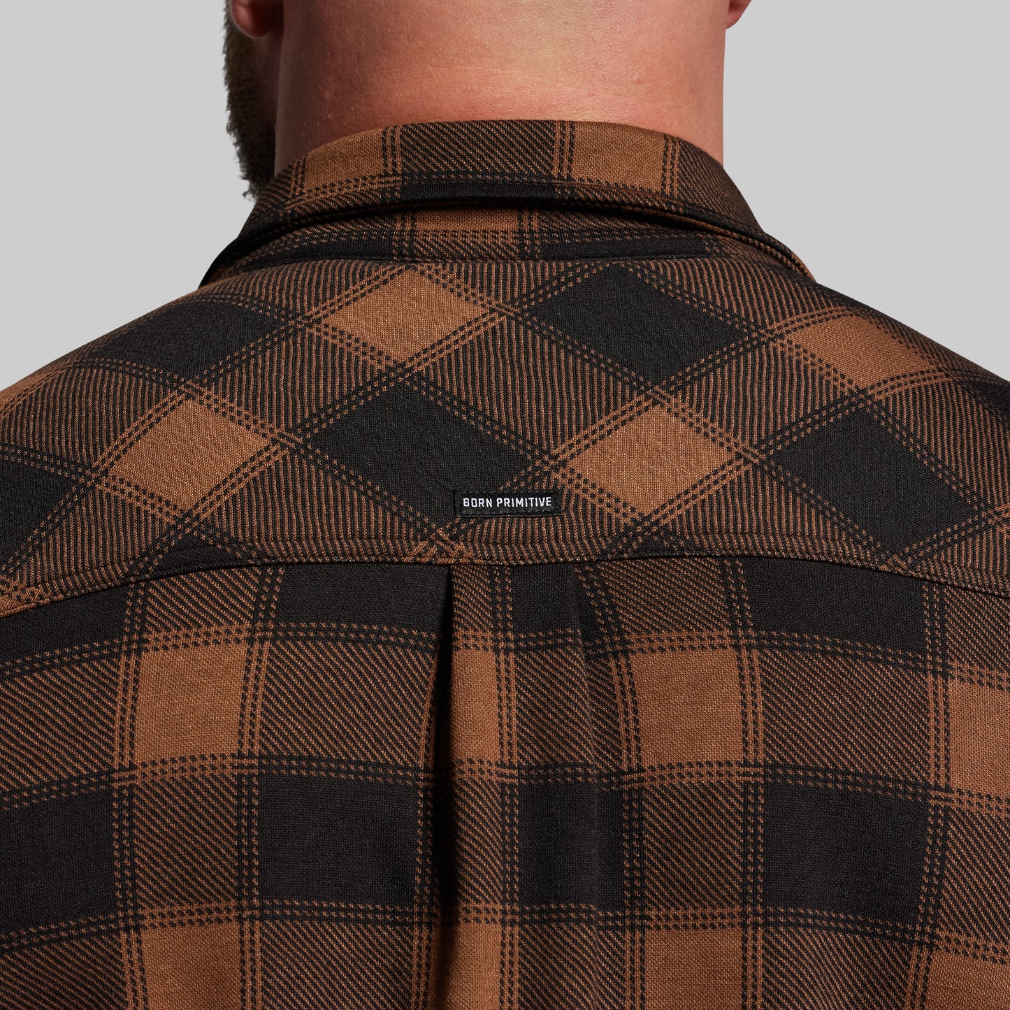 Brown and black plaid shirt with 'Born Primitive' label on a gray background