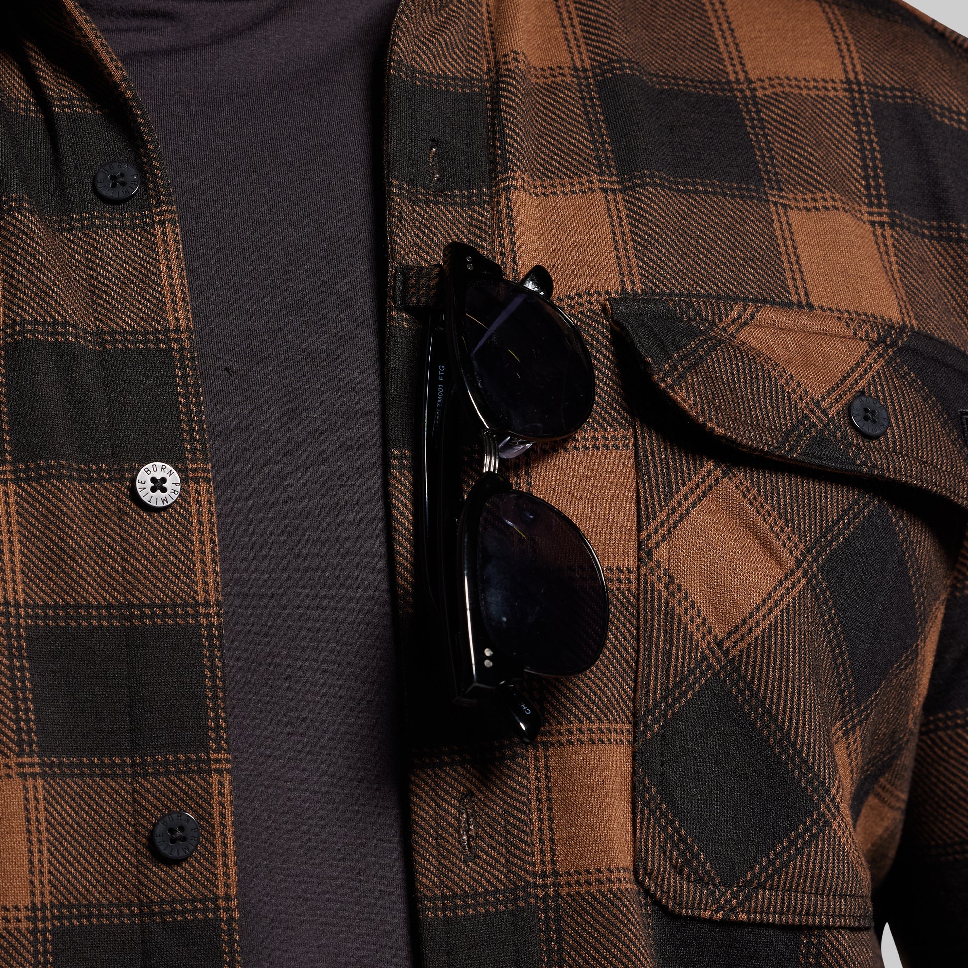Brown and black plaid shirt with sunglasses hanging on sunglass loop