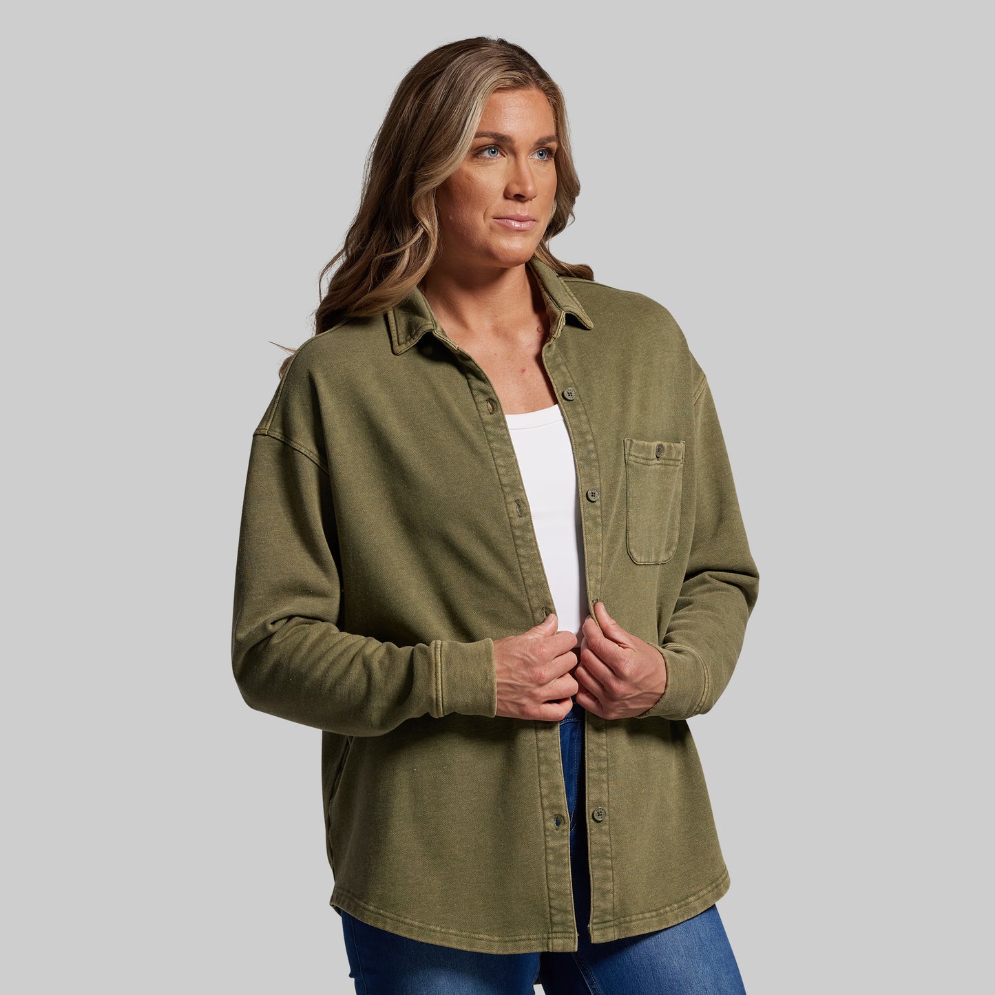 Woman wearing an olive green shirt over a white top on a gray background
