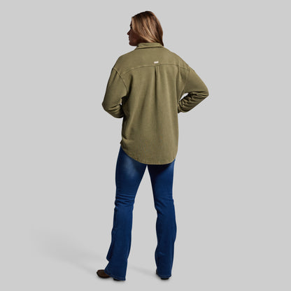Person wearing an olive green shirt and blue jeans on a gray background