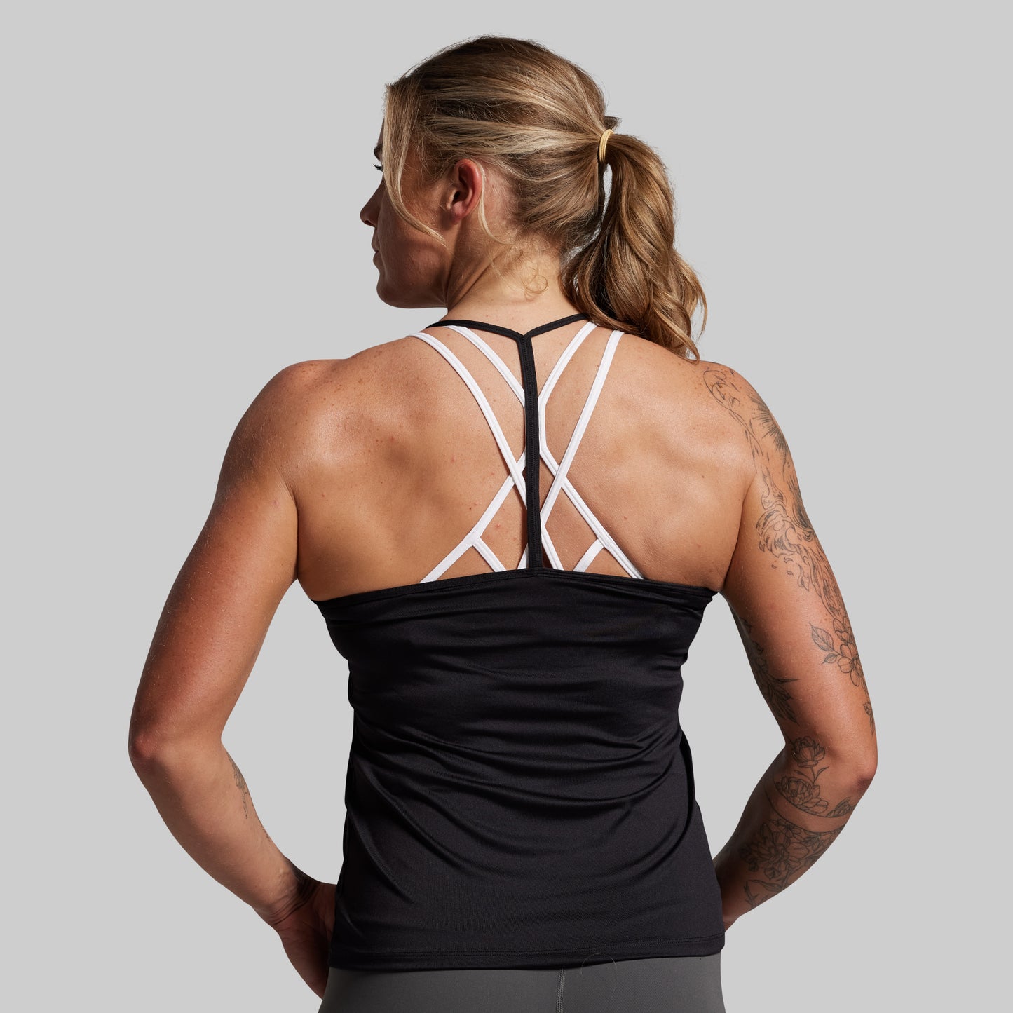 Woman wearing a black tank top with a unique back design on a gray background