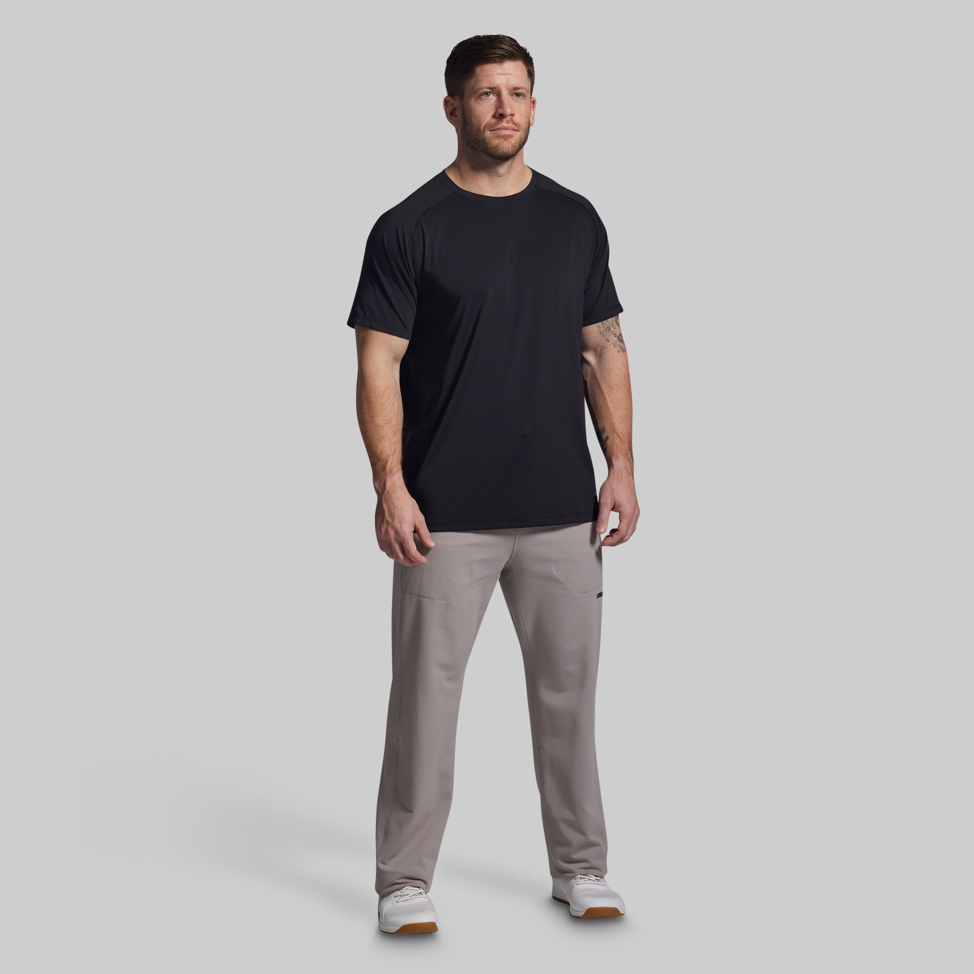 Man wearing a black t-shirt and gray pants on a light gray background