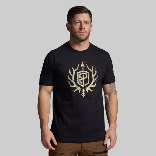 Man wearing a black t-shirt with a gold logo on a gray background