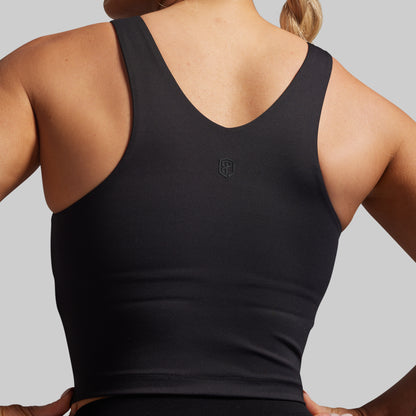 Person wearing a black tank top with a logo on the back against a gray background