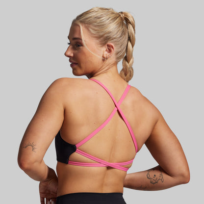 Woman wearing a black and pink sports bra against a gray background