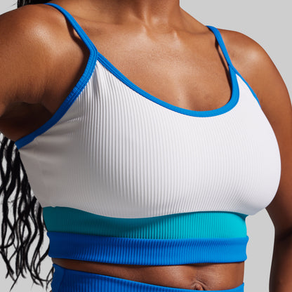 Person wearing a white and blue sports bra with a matching blue bottom on a gray background