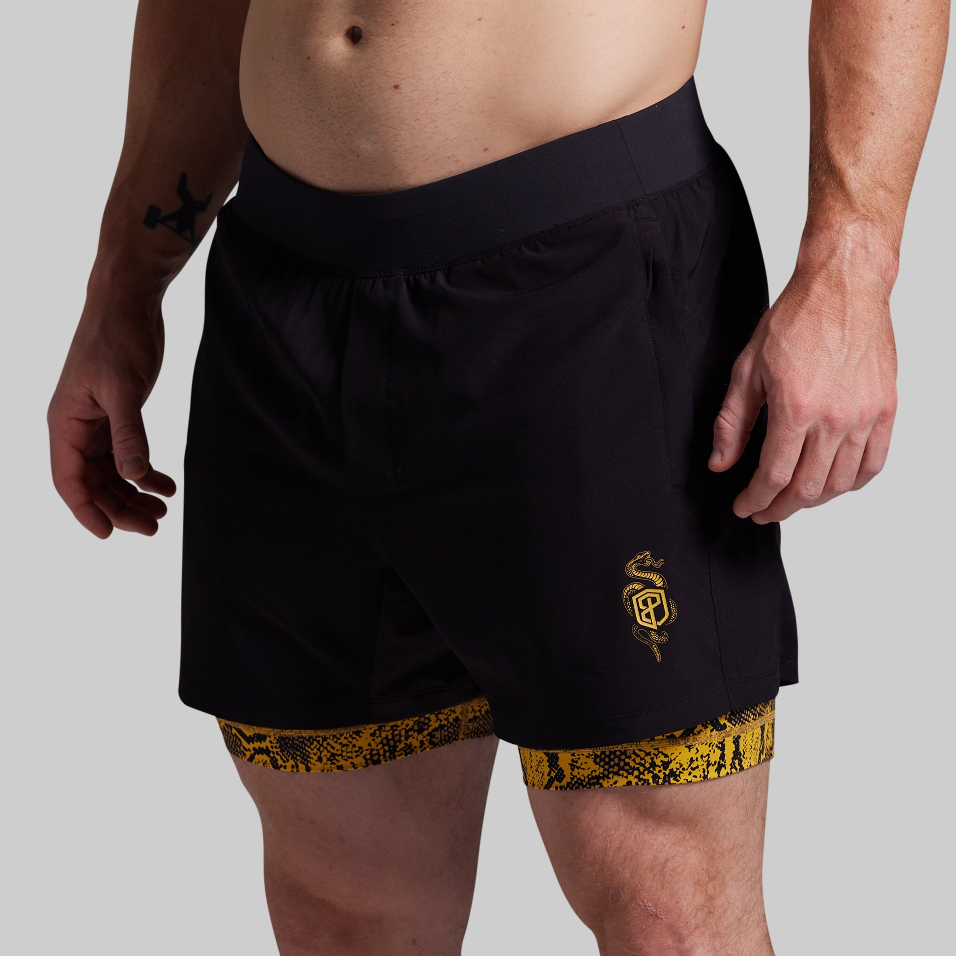 Black athletic shorts with yellow patterned lining worn by a person on a gray background